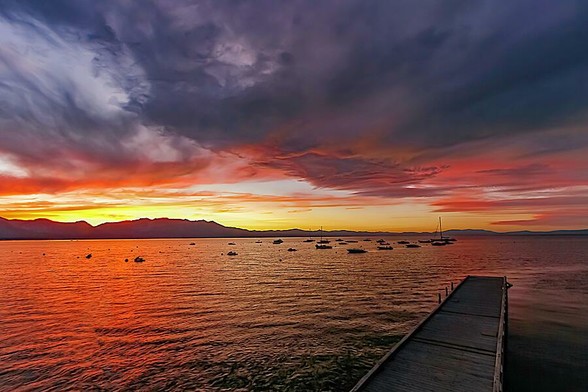 Last Light Lake Tahoe

Last Light Lake Tahoe is an image I captured while visiting Lake Tahoe. 
In the foreground is a dock that runs out towards right edge of the image. The lake color changes from a dark blue to a reddish/orange color. 
The silhouette of the mountains split the lake and the sky. 
The sky is a brilliant yellow at the horizon that fades to orange and then blue. 
Out on the lake there are some boats moored out at their buoys.