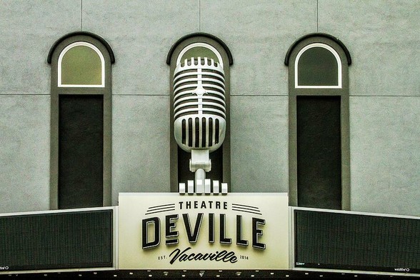 Theatre DeVille

Captured in downtown Vacaville, California, this is the Theatre DeVille. Remodeled in a art deco style the building stands out proudly on Main Street.
The bottom of the image is the marquee of the building. The name of the theatre sits prominently front center of the marquee. The building is painted in various shades of gray and black. The sign has been given a slight yellowish tint to give it an aged look. 
On top of the marquee is a large replica of an old antique style microphone. 
There are three windows, one of which is blocked by the microphone. The windows are tall and narrow with an arch at the top.