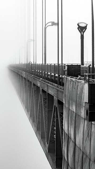 Golden Gate Bridge Portrait

This is a black and white image of the Golden Gate Bridge spanning the San Francisco Bay.
This was captured from the walkway that goes around the north tower of the bridge.  The view is looking south towards the city. 
I was able to reach out over the bridge to get this angle.
The bridge enters the image from the lower right corner and works across over to the left center of the image. You can clearly see the steel girders under the bridge and the cables that hold the bridge deck in place. 
The fog is so thick that all details disappear into the fog.