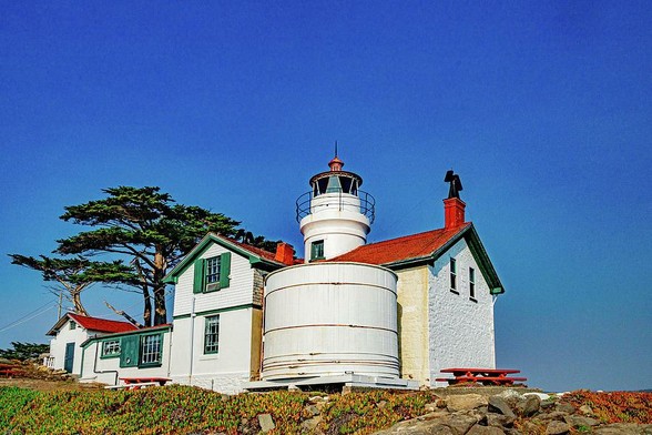 Battery Point Lighthouse II

This is an image of the Battery Point Lighthouse located in Crescent City, California. 
I was part way down the hill in between the lighthouse and the ocean when I captured this image.
The immediate foreground are some ice plants that grow around the lighthouse.
Above the ice plants is a large water storage tank made of wood and painted white with steel straps holding it together. Directly above the water tower is the light.
The lighthouse is painted white with green trim. The roof is red shingles. There is a coastal cypress tree behind the lighthouse and the sky is clear and deep blue.