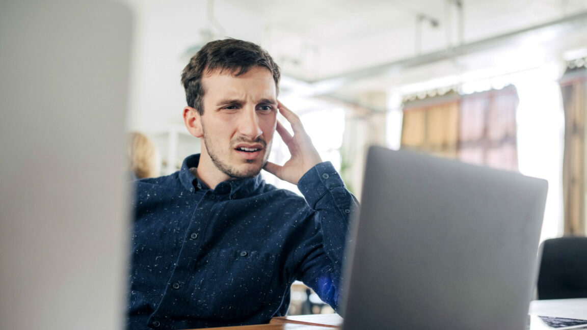 Confused businessman looking at laptop while sitting at desk in office