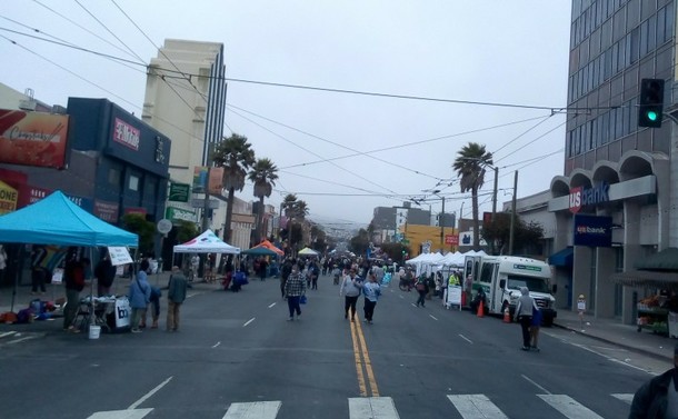A crowd of people stretching back for blocks along a street closed to traffic. There are dozens of booths.