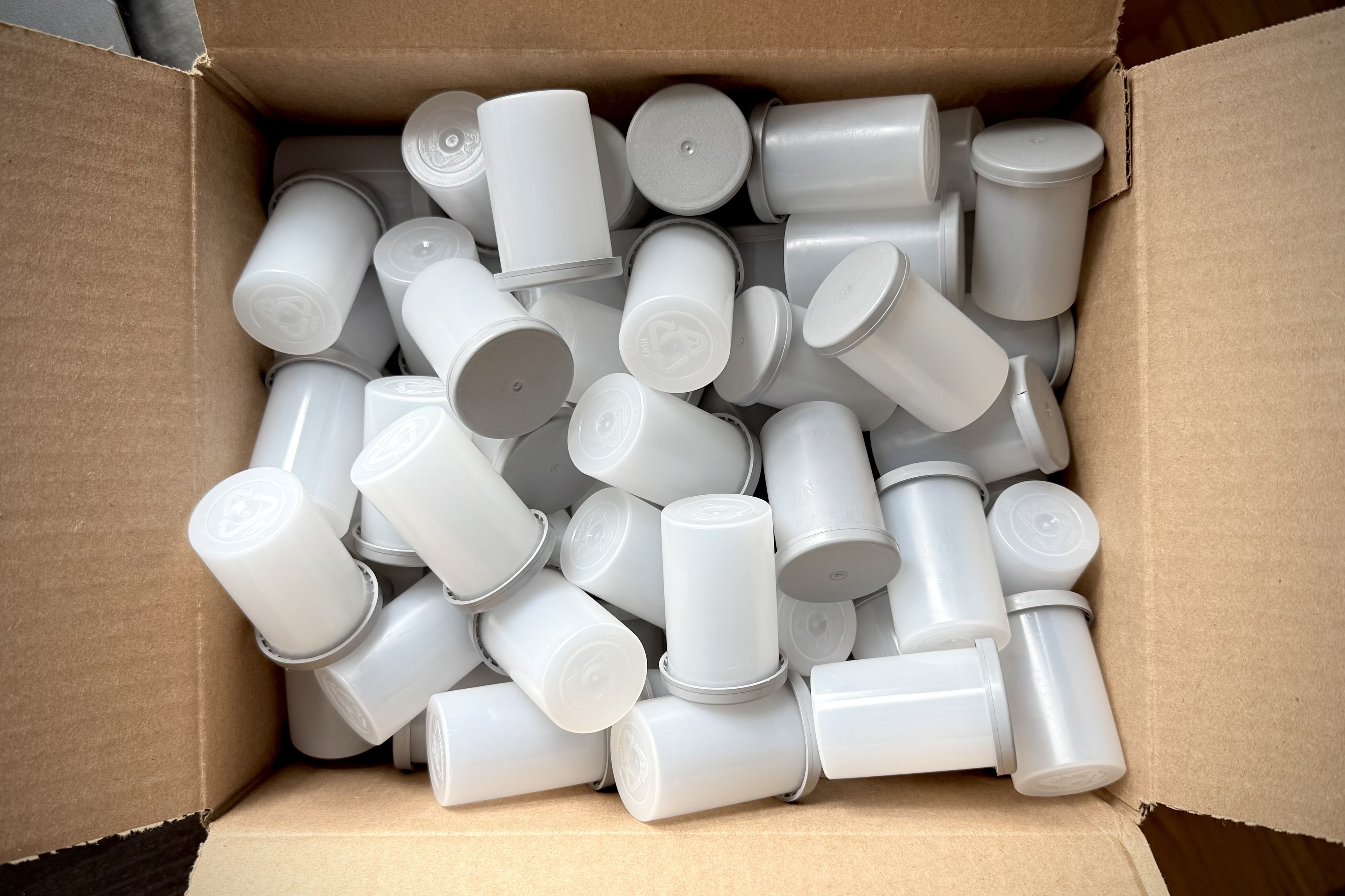 Looking down on a cardboard box full of empty white 35mm film canisters with gray lids