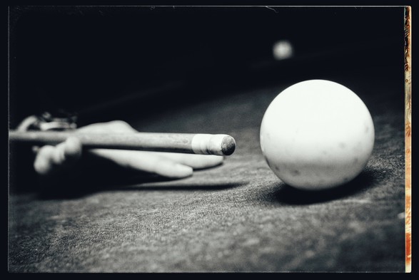 A monochrome picture of a cue stick about to hit the cue ball... In a darkened bar on a table only lit by a single bulb from a lantern above the center of the pool table. 

There is no sunset or flower in this picture.