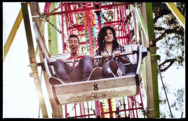 A young couple on a Ferris wheel ride. He clearly has joy in his expression and she is smugly happy.

Photographed from below the edge of the ride. With sun glaring and jelly bean colors all around. It is a sweet moment.