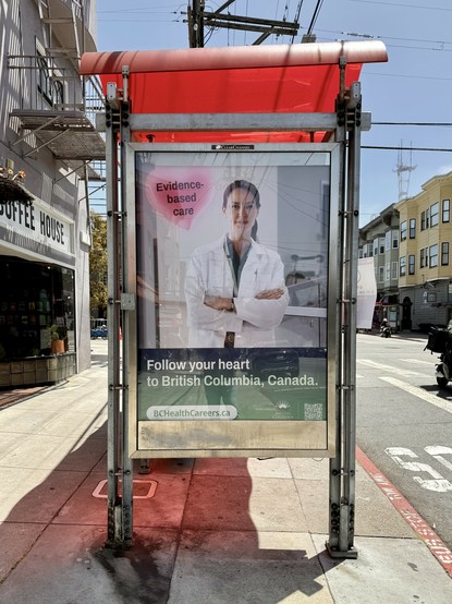 Photograph of a bus shelter in an urban streetscape. An ad on the shelter depicts a person wearing a white doctor’s robe and the headlines “Evidence-based care” and “Follow your heart to British Columbia, Canada.”