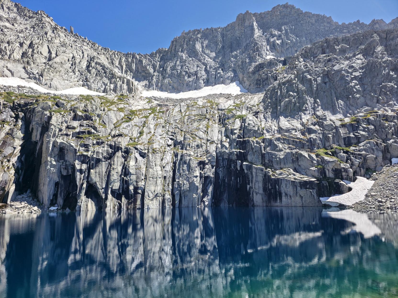 Tall cliff faces reflect in an alpine lake beneath a high peak