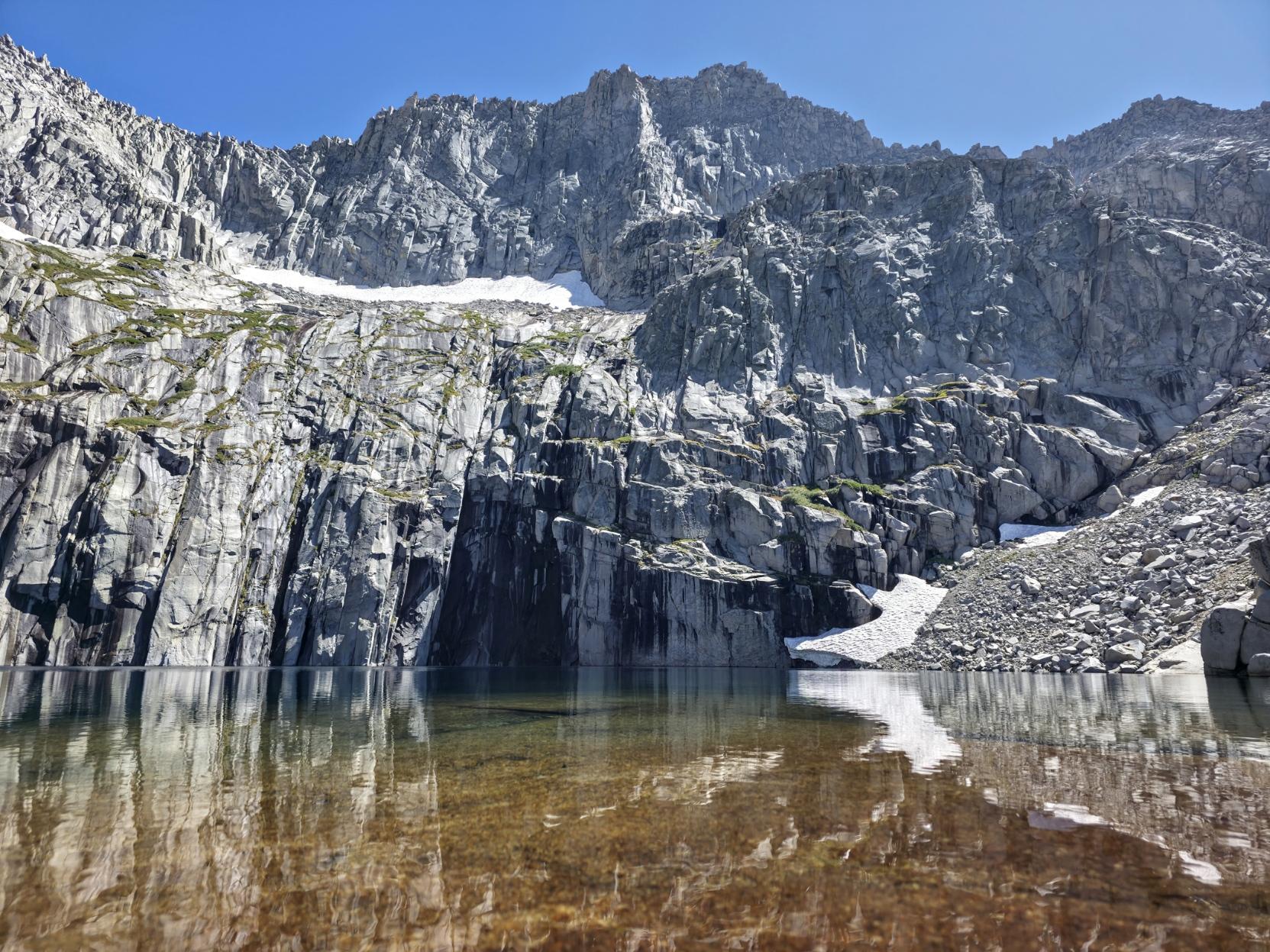 Tall cliff faces reflect in an alpine lake beneath a high peak