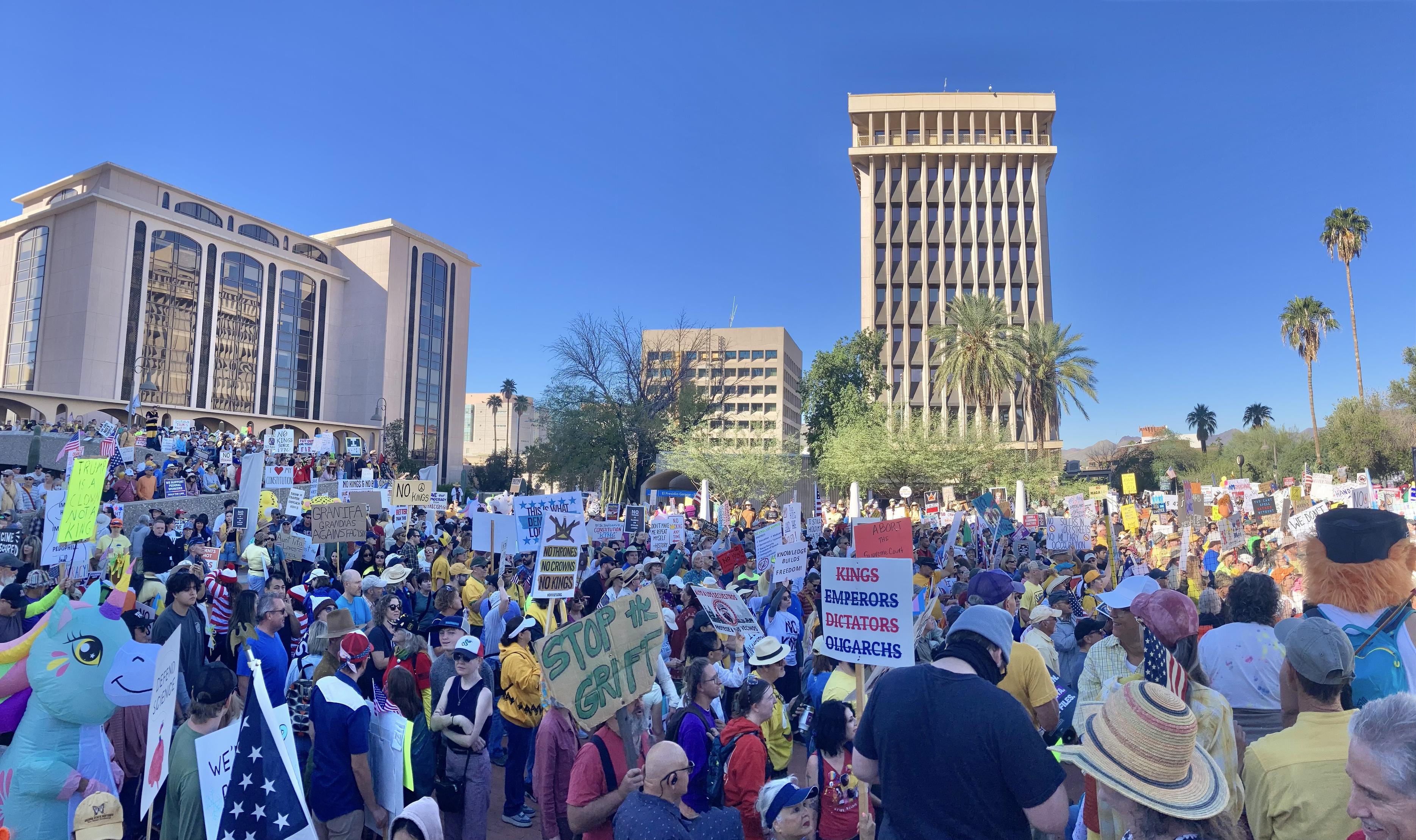 A large crowd of people holding a mix of progressive and anti-Trump protest signs.