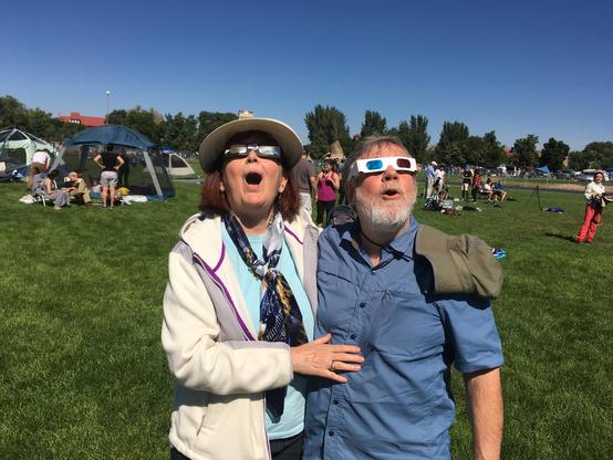 Two people preparing to look at a total solar eclipse.  One is wearing protective glasses, the other is wearing red/blue 3-D glasses.