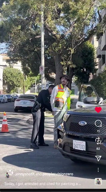 A man is being handcuffed by a cop. The cop tells people watching the arrest that they're vandalizing city property and will all go to jail if they don't back up. Later, sitting on a bench, the man explains the crosswalk painting project and there's some footage of crosswalks being painted.