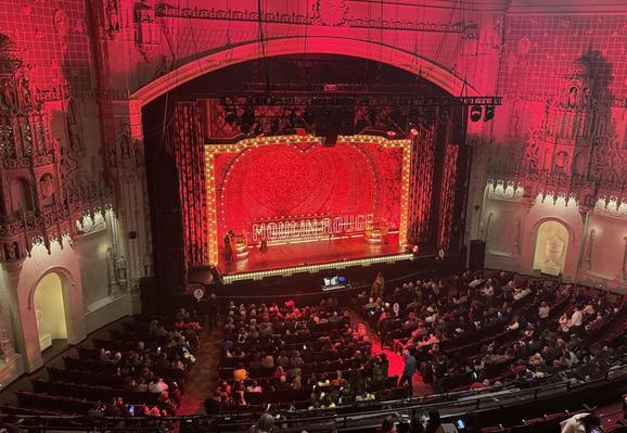 Orpheum Theatre stage viewed from the balcony area. Awash in red lighting with bright red sign saying Moulin Rouge 