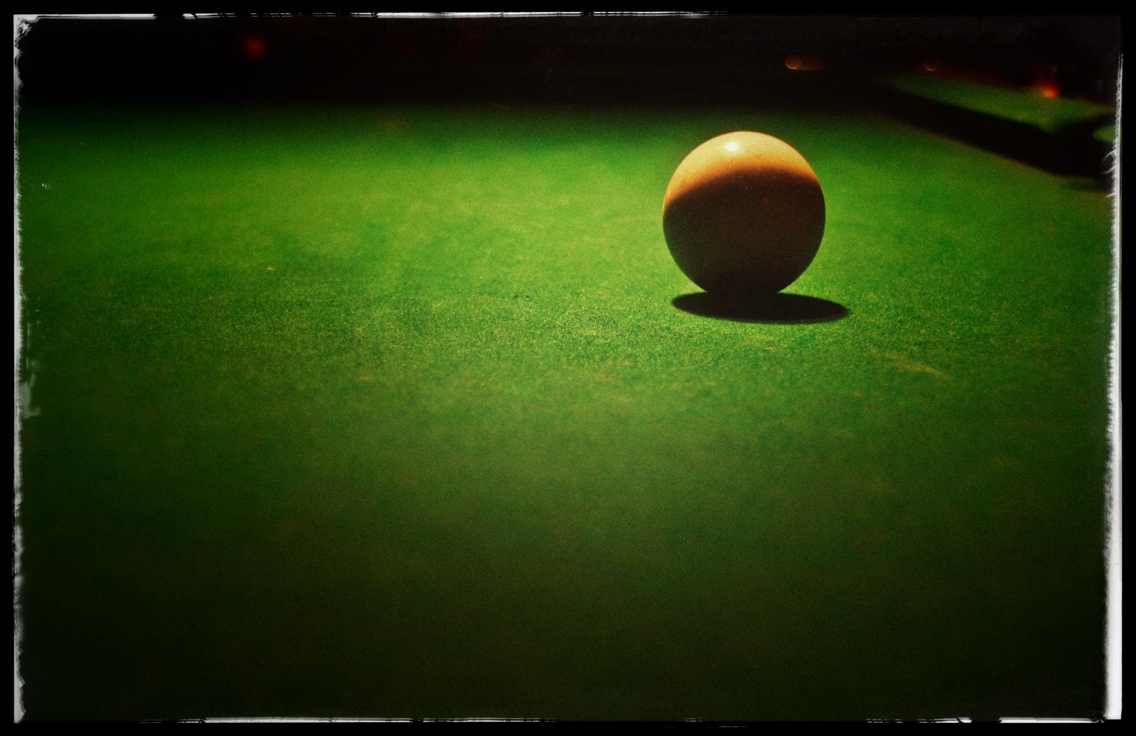 The most minimal photo I think I've ever taken: a one-ball (the yellow one) sitting alone, on the green felt of a pool table, in a puddle of light from an overhead lamp, in an otherwise completely dark bar. The ball is in focus. The rest of the photo, foreground and background, fades away in grainy bokeh and darkness.