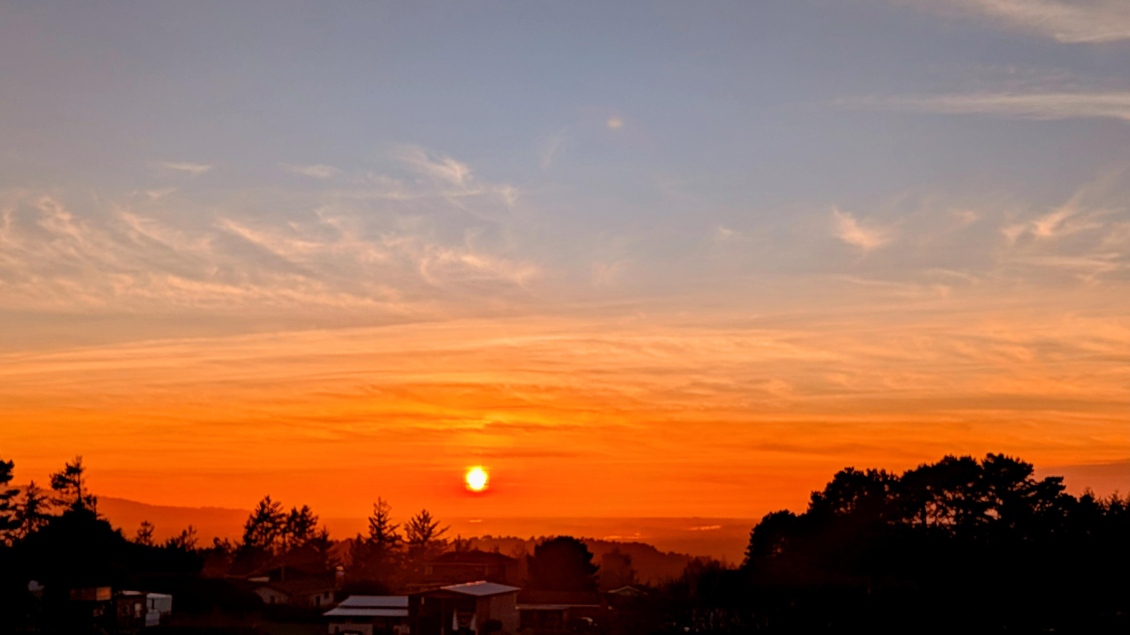 The clouds looked stacked or layered and orange around the sun at the end of the day. A little blue sky above. 
Dark tree tops at the bottom.